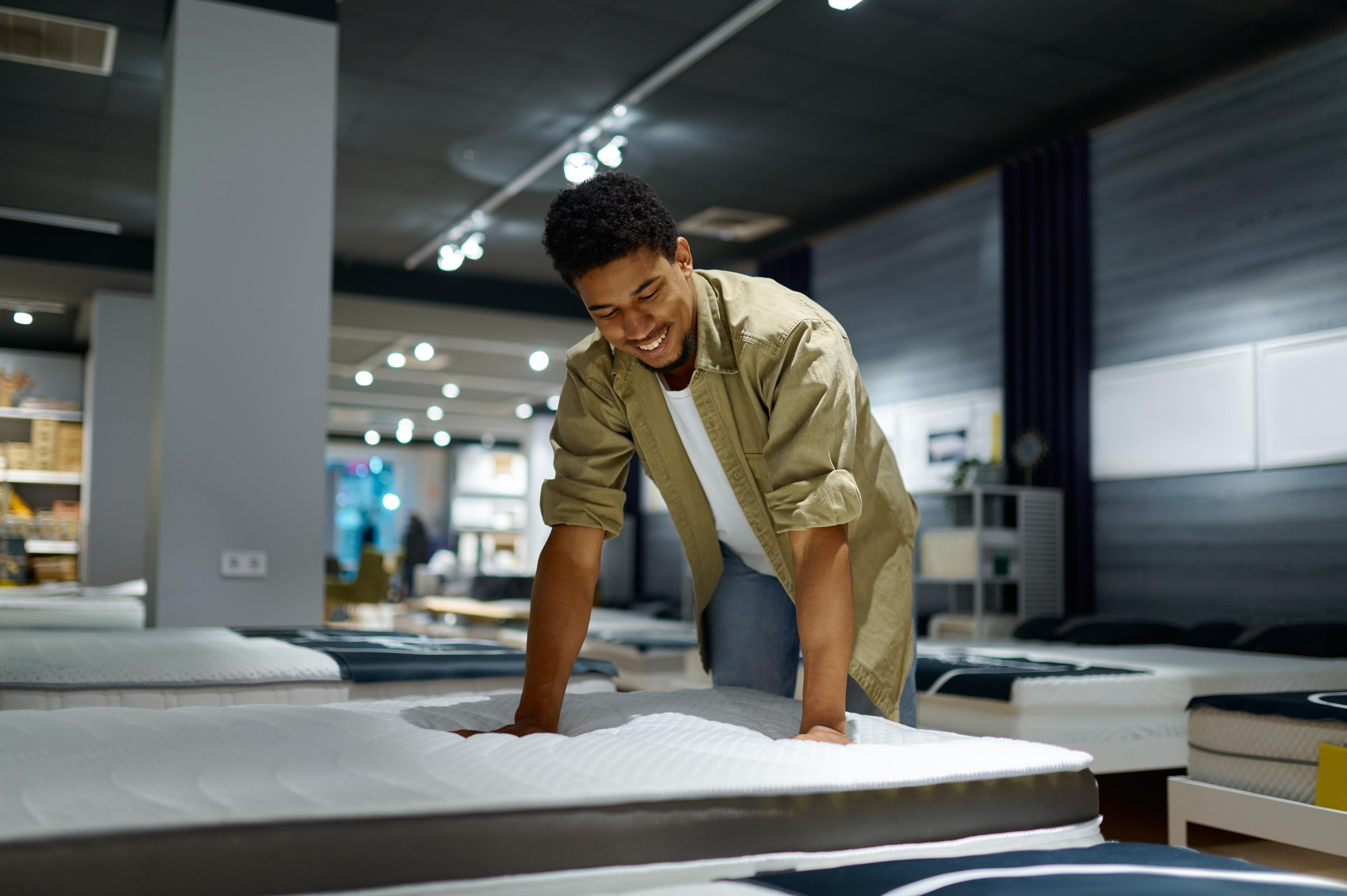 A customer checking out the material of a mattress in a store. He appears happy with the mattress he found and is looking to shop using his lease approval amount.