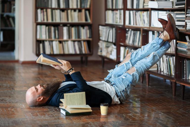 A man reading a book while propping his feet on a bookshelf