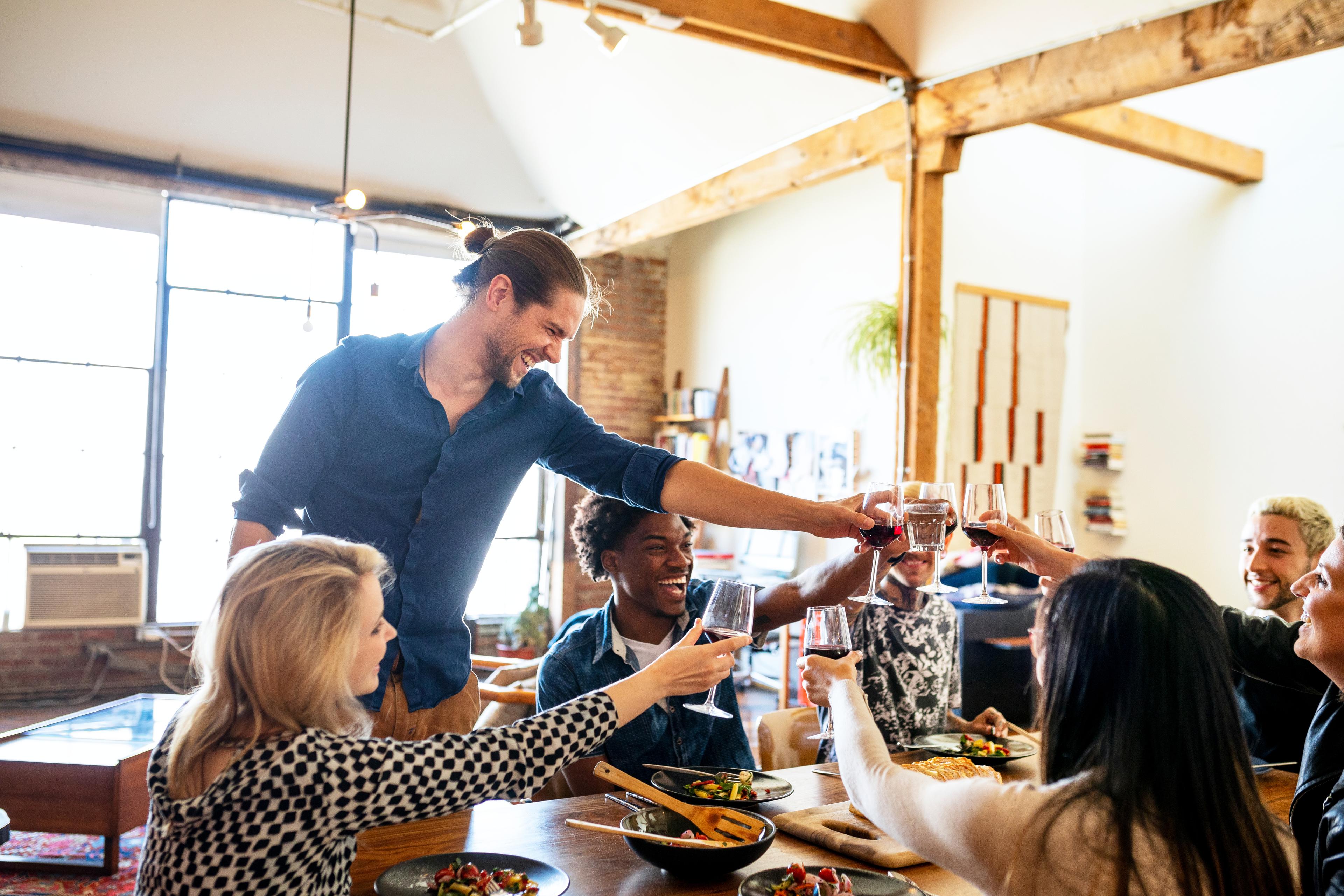 A group of happy people are surrounding a dining room table in a home while celebrating a housewarming. 