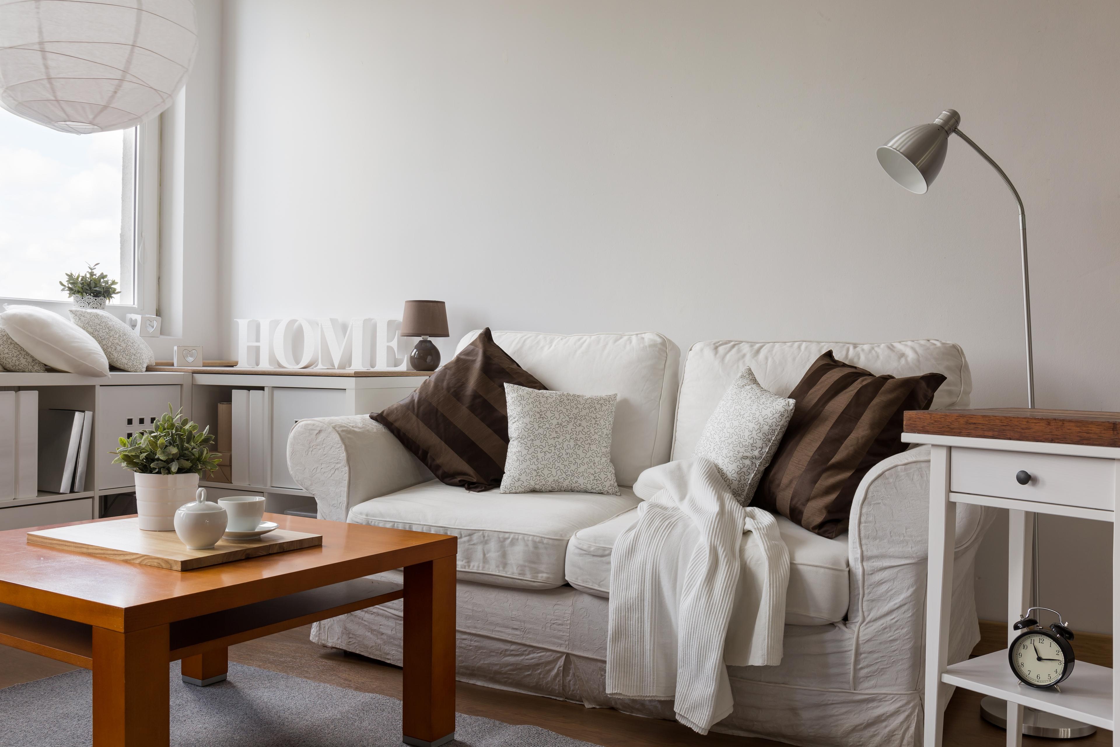 A welcoming home scene: sofa, coffee table, lamp, and bright natural light through open window create cozy ambiance.