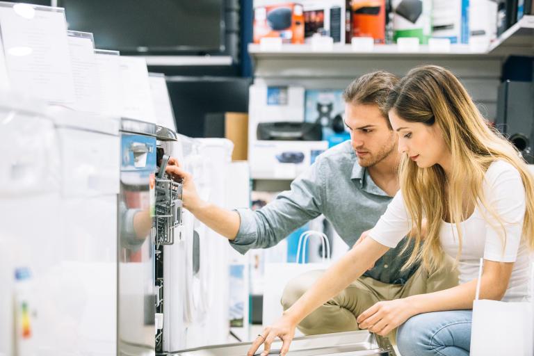 A view of a couple happily shopping in a store for an appliance and learning about different options for their shopping experience. 