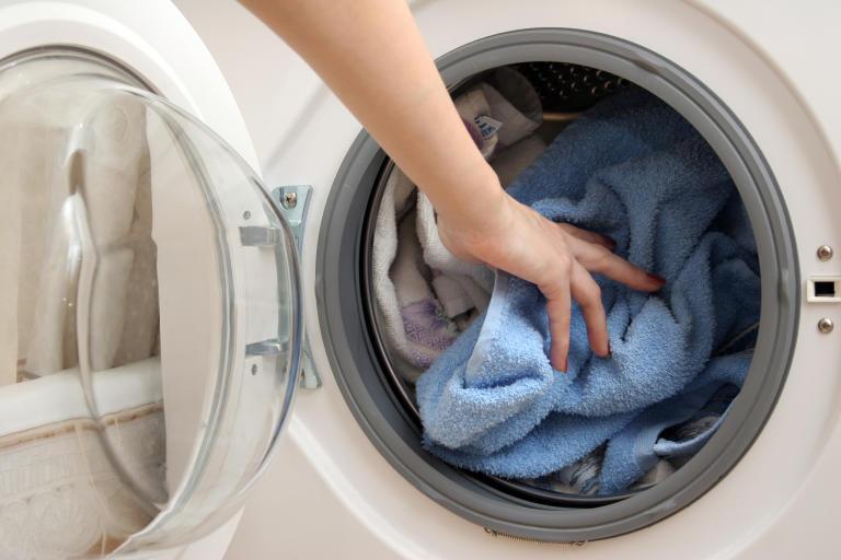 A person is reaching into a washing machine to pull out clothes.