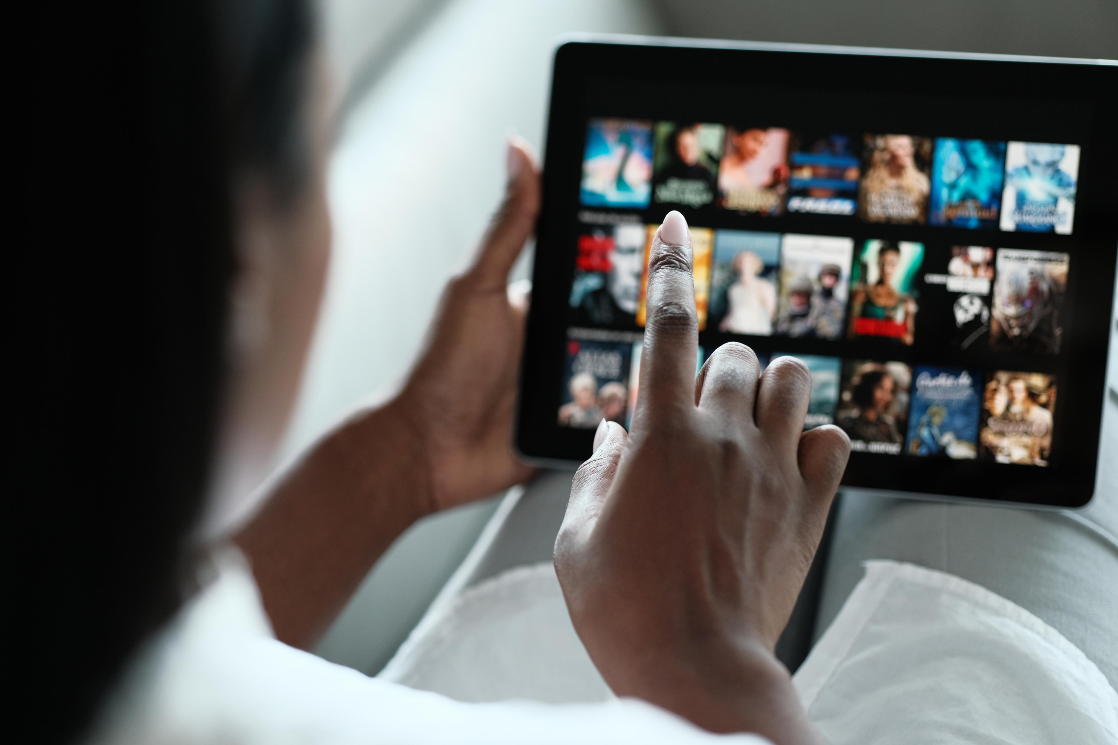 A person's finger hovers over a touchscreen, poised to select a streaming service for entertainment. The screen displays various streaming service logos, suggesting a multitude of options for viewing content on an electronic device.