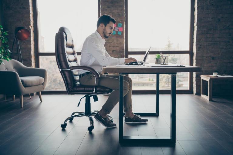 A young adult seated comfortably in an office chair, maintaining a stable and balanced posture in a productive working environment.