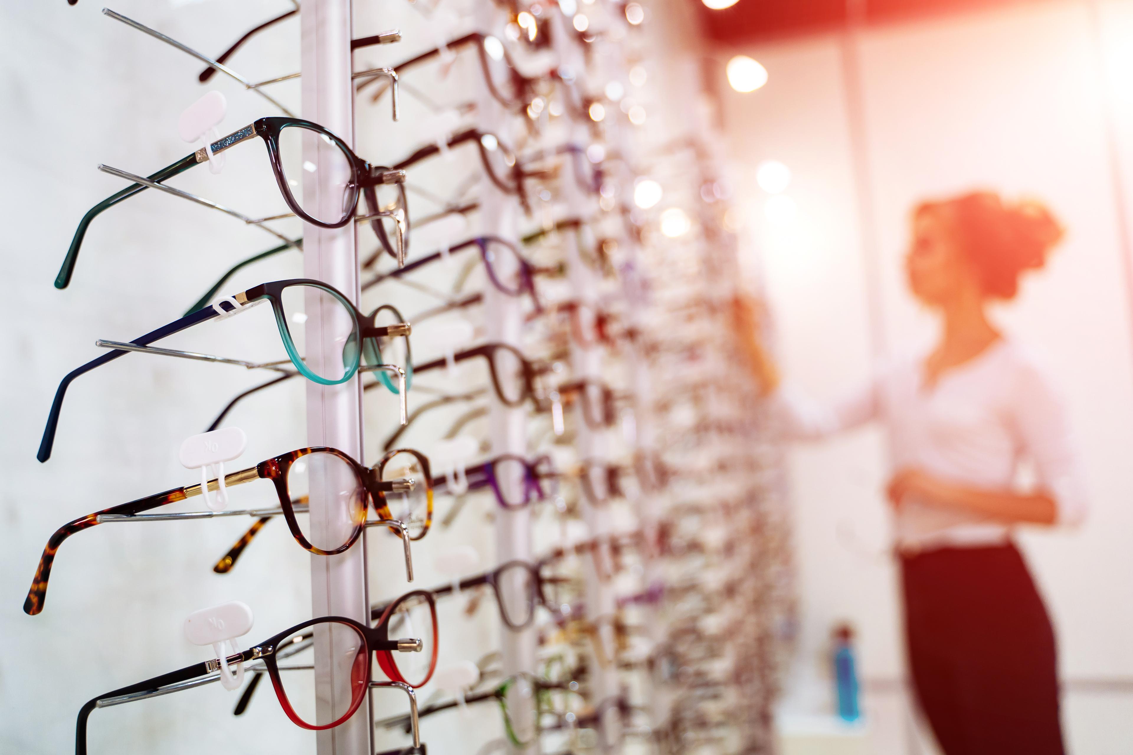 A view of the inside of an eyewear store with a customer looking at the options available to shop from.